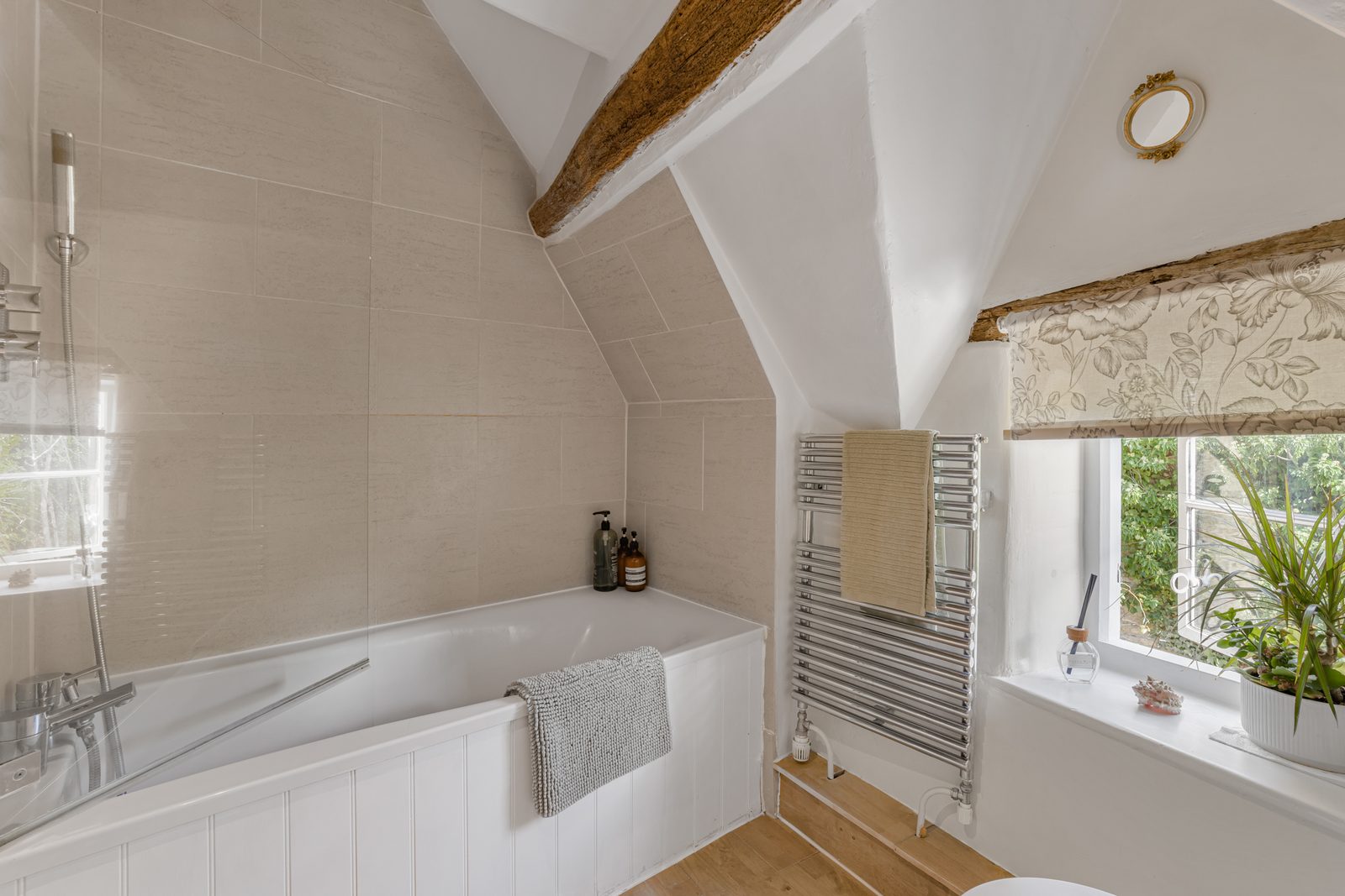 Bathroom at Green Hideaway with bath under the eaves, exposed beams and a window of plants