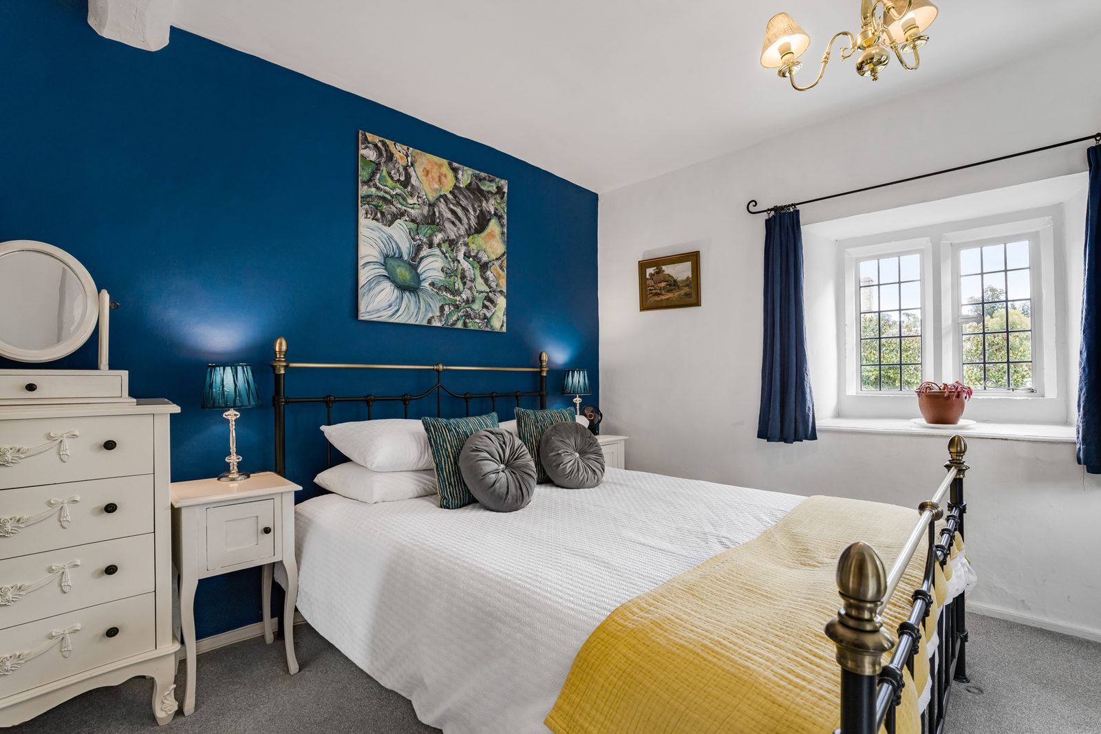 Blue bedroom at Riverside Cottage with brass bedstead and painted chest of drawers