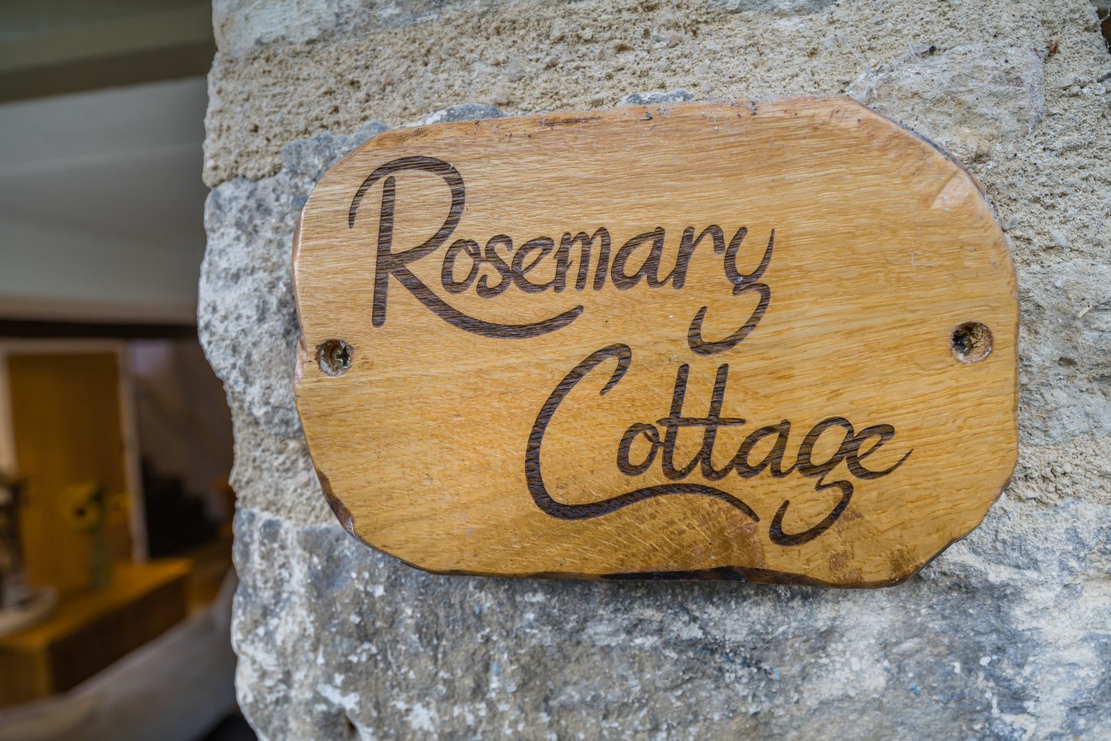 Carved wooden Rosemary Cottage sign fixed to the Cotswold stone wall